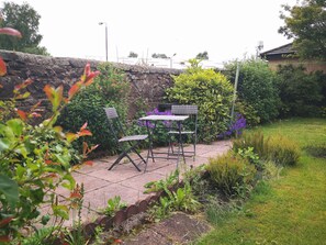 Een terras met tafel en stoelen, omgeven door weelderige beplanting en een stenen muur.