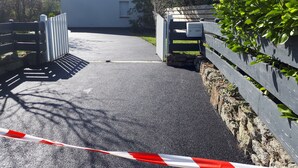 A gated driveway leading to a building with a white exterior and a small window.