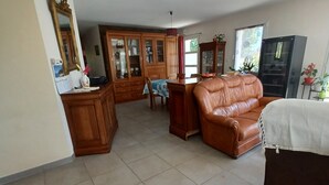A spacious living room with a brown leather sofa, a dining table with chairs, and a wooden cabinet with glass doors.