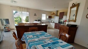 A dining area with a table covered in a patterned tablecloth, wooden chairs, and a small dog.