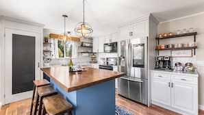 A modern kitchen with white cabinets, a wooden island, stainless steel appliances, and a blue rug.
