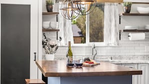 A modern kitchen with a wooden island, a wine bottle, glasses, and a fruit platter.