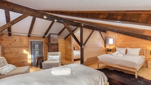 A cozy attic bedroom with two beds, a chair, and a wooden ceiling structure.