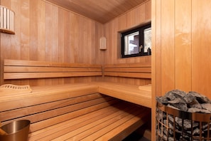 A wooden sauna with benches, a window, and a stone wall.