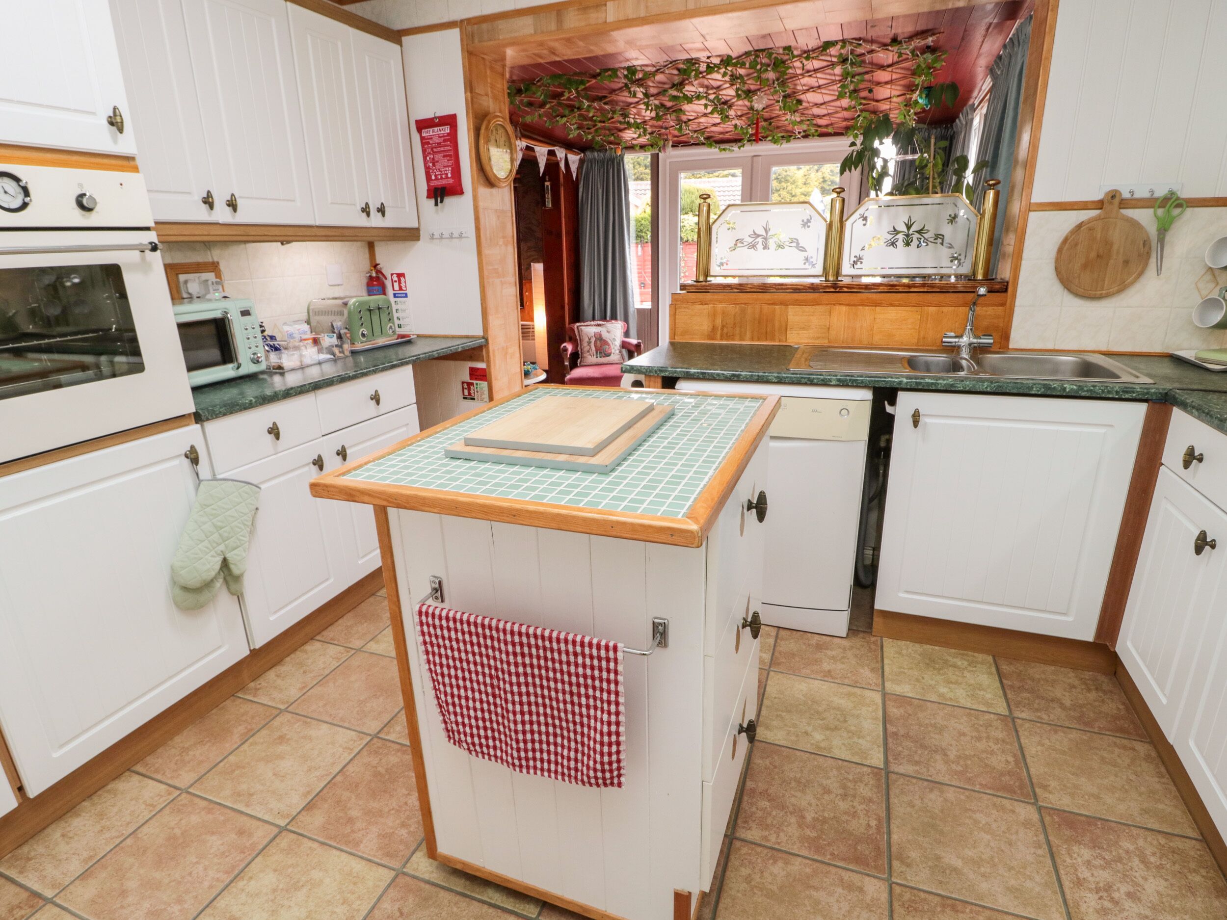 A kitchen with white cabinets, a green countertop, a wooden island with a cutting board, and a red and white checkered towel hanging from the island.