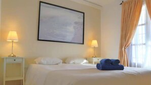 Ein Hotelzimmer mit Bett, zwei Nachttischlampen, einem gerahmten Kunstwerk an der Wand und einem Fenster mit Vorhängen.