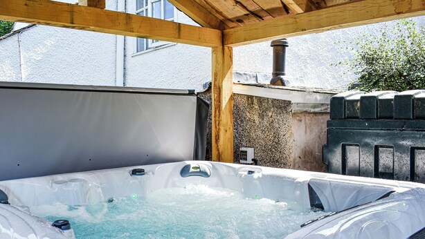Un bain à remous doté d’une structure de toit en bois, d’un mur en pierre et d’un réchauffeur en métal.