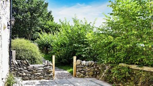 Un chemin de pierres menant à une porte en bois, entouré d’une végétation luxuriante et d’un mur de pierres.