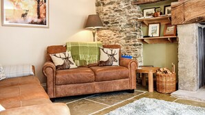 Un salon chaleureux avec un mur en pierre, un canapé en cuir marron agrémenté de coussins à motifs de cerfs, une lampe et une cheminée.