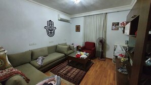 Ein Wohnzimmer mit einer Couch, einem roten Sessel, einem Couchtisch, einem Ventilator und einem kleinen Teppich.