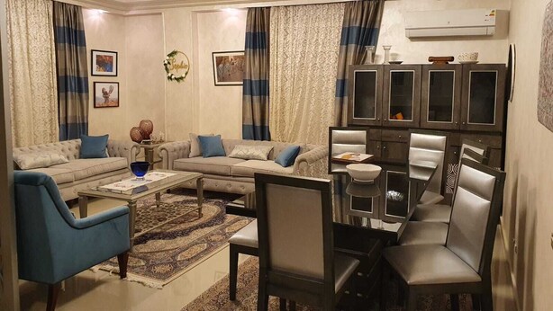 Ein Wohnzimmer mit einer Sofagarnitur, einem Couchtisch, einem Esstisch mit Stühlen und einer Vitrine mit Glastüren.