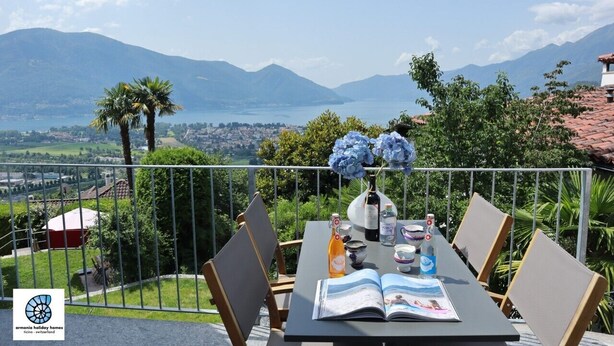 A balcony with a table set for two, overlooking a mountainous landscape and a body of water. - Casa Teatro Panoramico (Locarno)
