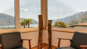A room with two black chairs, a wooden sculpture, and a large window with a mountain and lake view. - Casa Teatro Panoramico (Locarno)