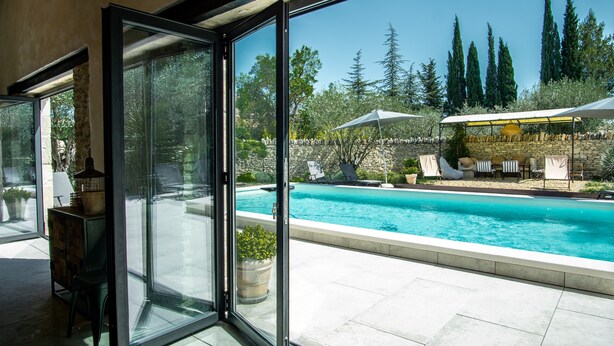 Una vivienda moderna con un ventanal que da a una zona de piscina, paredes de piedra y mobiliario exterior.