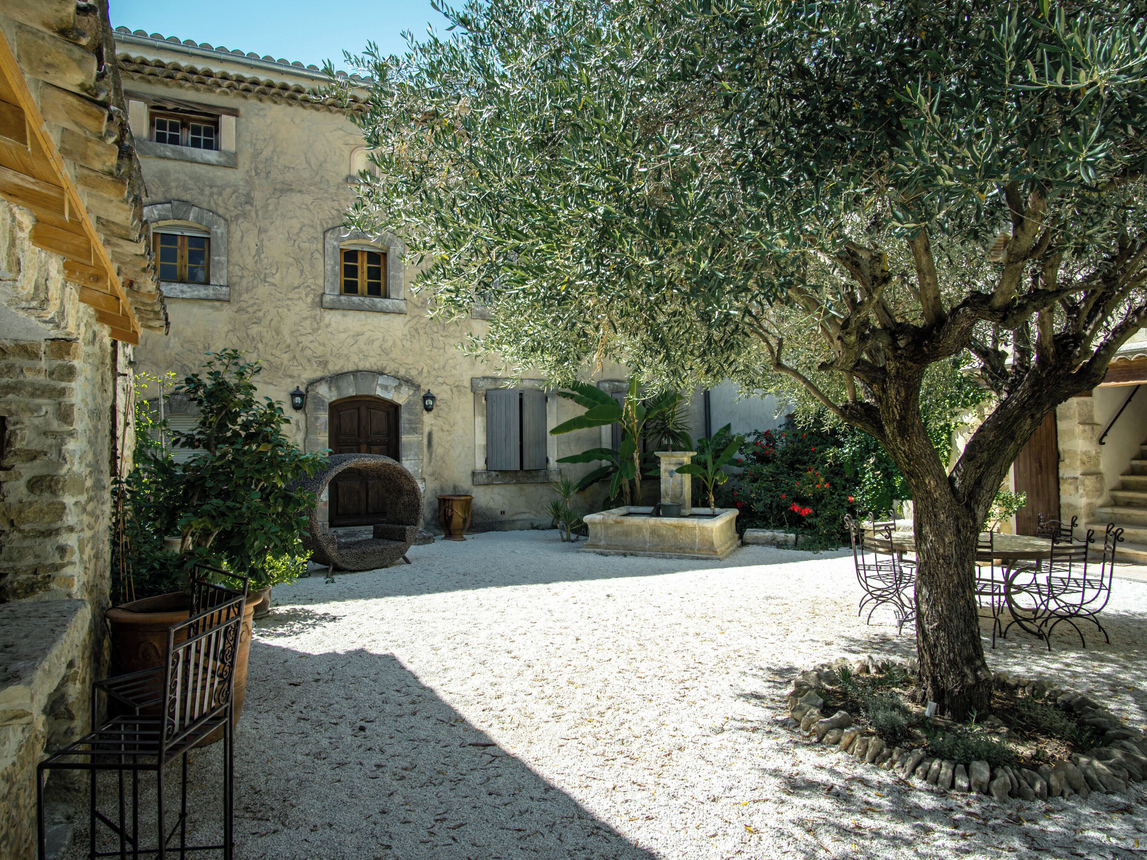 A courtyard with a stone building, a tree, and a fountain.