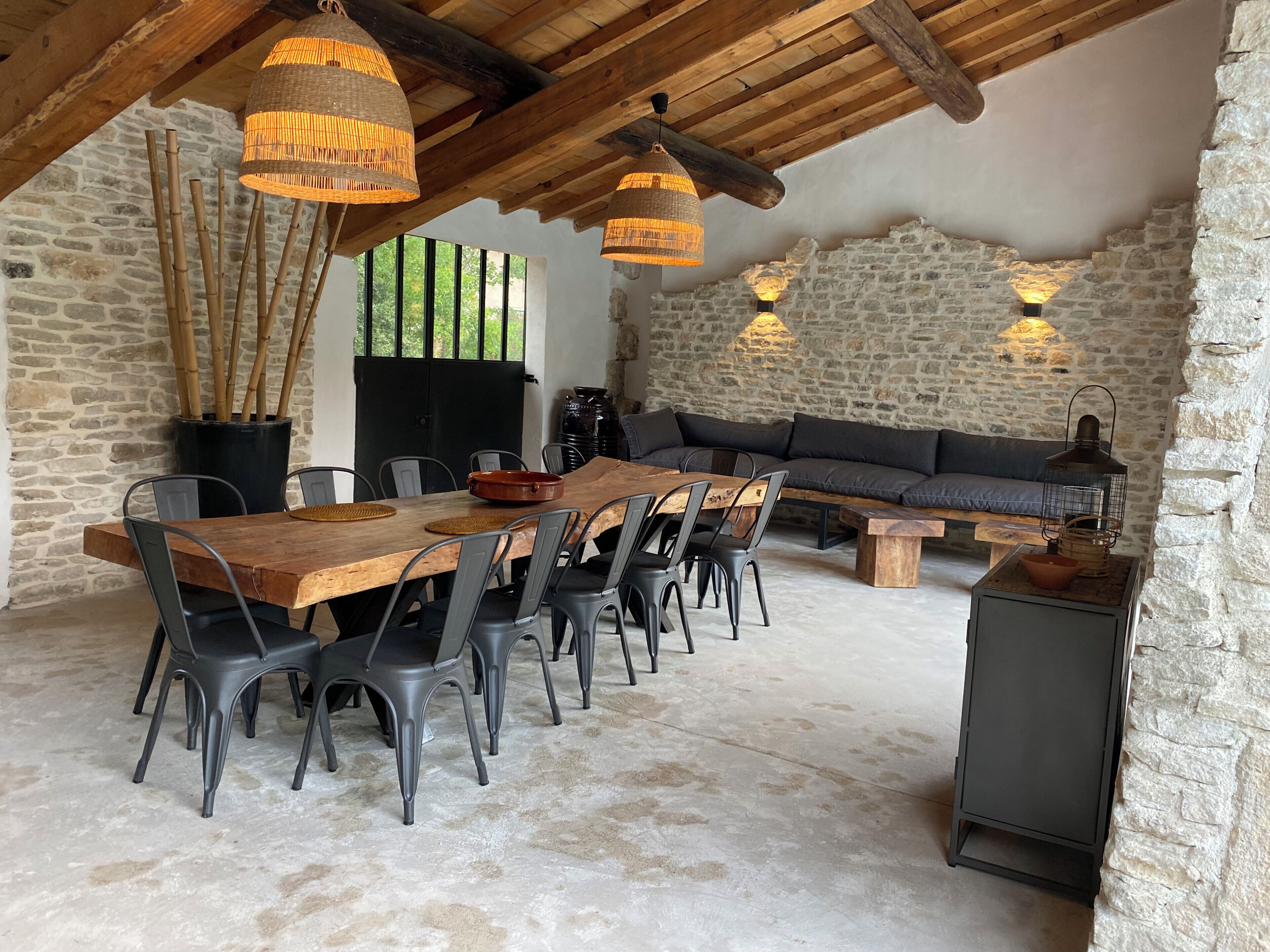 A rustic dining area with a long wooden table, black chairs, and woven light fixtures.