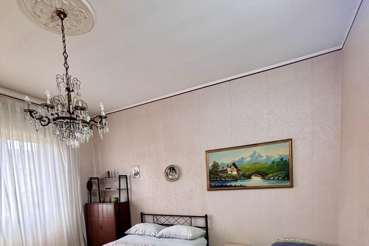 A bedroom with a bed, a smaller bed, a chandelier, a painting, and a wardrobe.