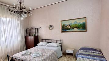 A bedroom with a bed, a smaller bed, a chandelier, a painting, and a wardrobe.