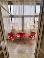 Un balcone con tavolo e due sedie, vista sugli edifici e una tenda.