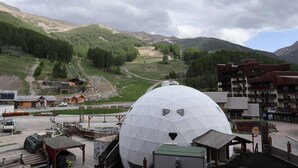 Une grande structure en forme de dôme blanc, vraisemblablement un observatoire scientifique, est entourée d’un paysage montagneux. On aperçoit au premier plan un petit bâtiment et une zone de stationnement.