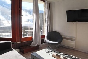 A modern room with a large window, a flat-screen TV, a comfortable chair, and a small table with a candle holder. - 15m from ski slopes, 3rd floor, balcony, 24m², Les Orres (Les Orres)