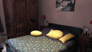 Ett sovrum med ett blommigt sängöverkast, en garderob i trä, ett nattduksbord med en lampa och en tavla på väggen.