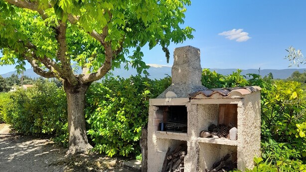 En enkel grillplats utomhus, omgiven av grönska och under en klar himmel.