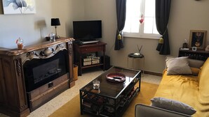 Ett vardagsrum med en TV, ett träskåp, en soffa, ett soffbord och konstverk på väggen.