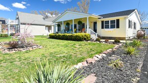 A single-story house with a porch, a small garden with a variety of plants, and a clear blue sky.