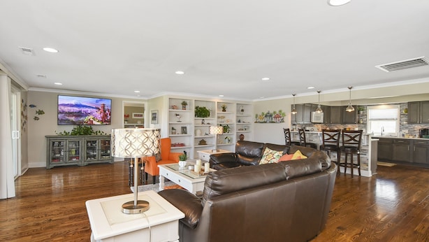 A spacious living room with a brown leather sofa, a white coffee table, and a TV mounted on the wall.