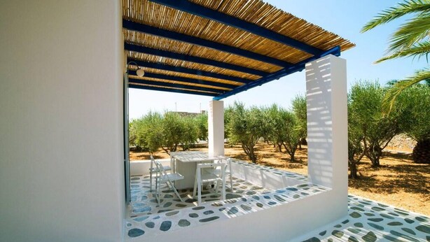 An outdoor patio with a table and chairs, surrounded by a stone floor and a thatched roof structure. - Aegean Villa in Paros (Paros)