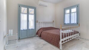 A bedroom with a bed, two windows, a radiator, and a white radiator cover. - Aegean Villa in Paros (Paros)