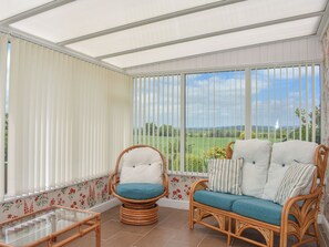 Una veranda con mobili in vimini, un tavolo in vetro e vista su un paesaggio verde.