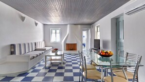 A modern living room with a checkered floor, a glass dining table with chairs, a sofa, and a fireplace. - Ocean Villa in Paros (Paros)