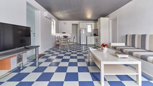 A modern living room with a checkered floor, a flat-screen TV, a sofa, and a dining area with chairs and a table. - Ocean Villa in Paros (Paros)