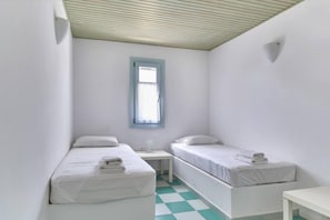 Una habitación pequeña y limpia con dos camas individuales, una mesita y una ventana con detalles azules.