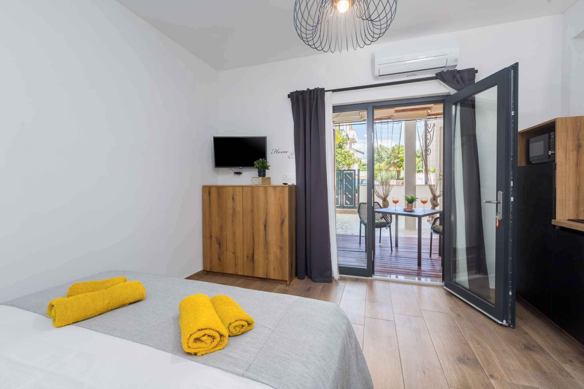 Ein Hotelzimmer mit einem Bett, einem Holzschrank, einem Fernseher und einer Glastür, die zu einem Außenbereich mit Tisch und Stühlen führt.