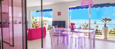 A modern living room with a dining area, large windows, and a view of the sea.
