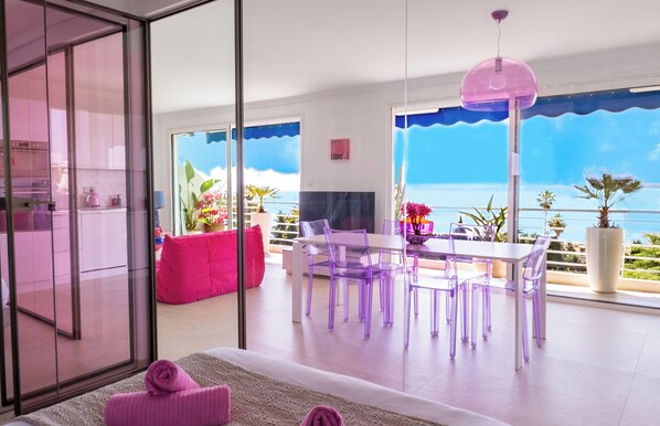A modern living room with a dining area, large windows, and a view of the sea.