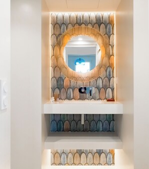 A bathroom with a mirror, a sink, and a decorative wall with a leaf pattern.