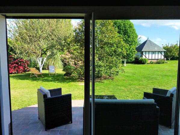 A patio with wicker furniture and a view of a well-maintained lawn and a Tudor-style building.