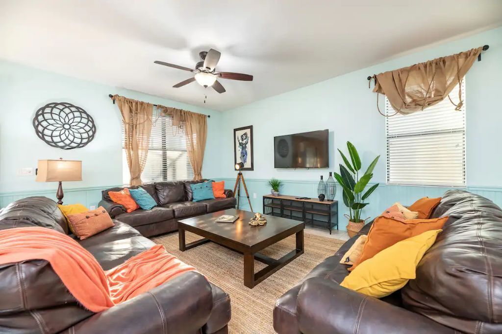 A living room with a sofa set, a coffee table, a ceiling fan, and a television.