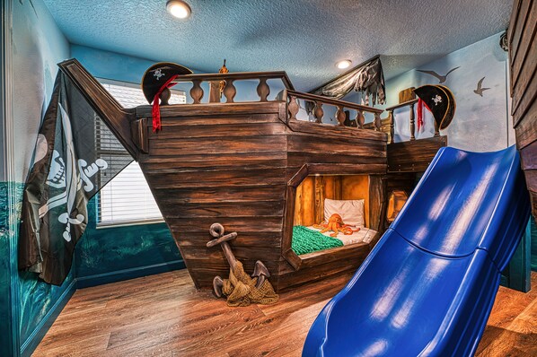 Un cuarto de juegos infantil con una cama litera de madera, un tobogán y decoración temática de piratas.