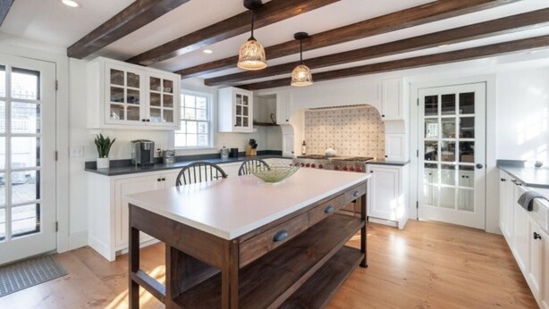 Une cuisine spacieuse avec des poutres en bois, des meubles blancs et des luminaires suspendus.
