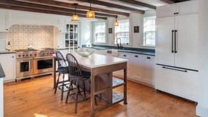 Une cuisine avec des poutres en bois, des meubles blancs, un îlot central et des luminaires suspendus.
