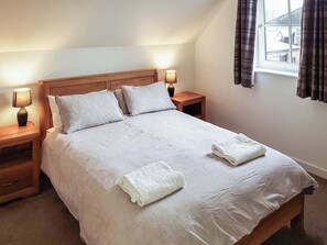 Un lit bien fait, avec du linge de lit blanc et deux serviettes, une tête de lit en bois, des lampes de chevet et une fenêtre avec des rideaux.