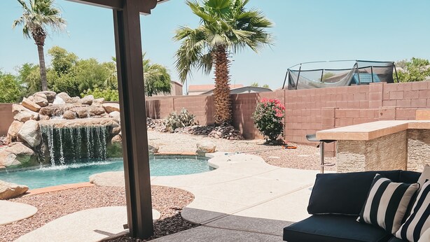 A covered outdoor seating area with a pool, palm trees, and a rock waterfall. - Resort Style Heated Pool close to Entertainment (Phoenix)