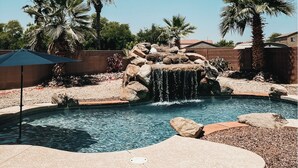 A swimming pool with a waterfall feature, surrounded by palm trees and a brick wall. - Resort Style Heated Pool close to Entertainment (Phoenix)