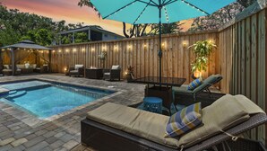 A backyard with a swimming pool, lounge chairs, and a wooden fence.