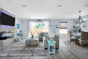 A spacious living room with a large TV, comfortable seating, a dining area, and a view of the outdoors.